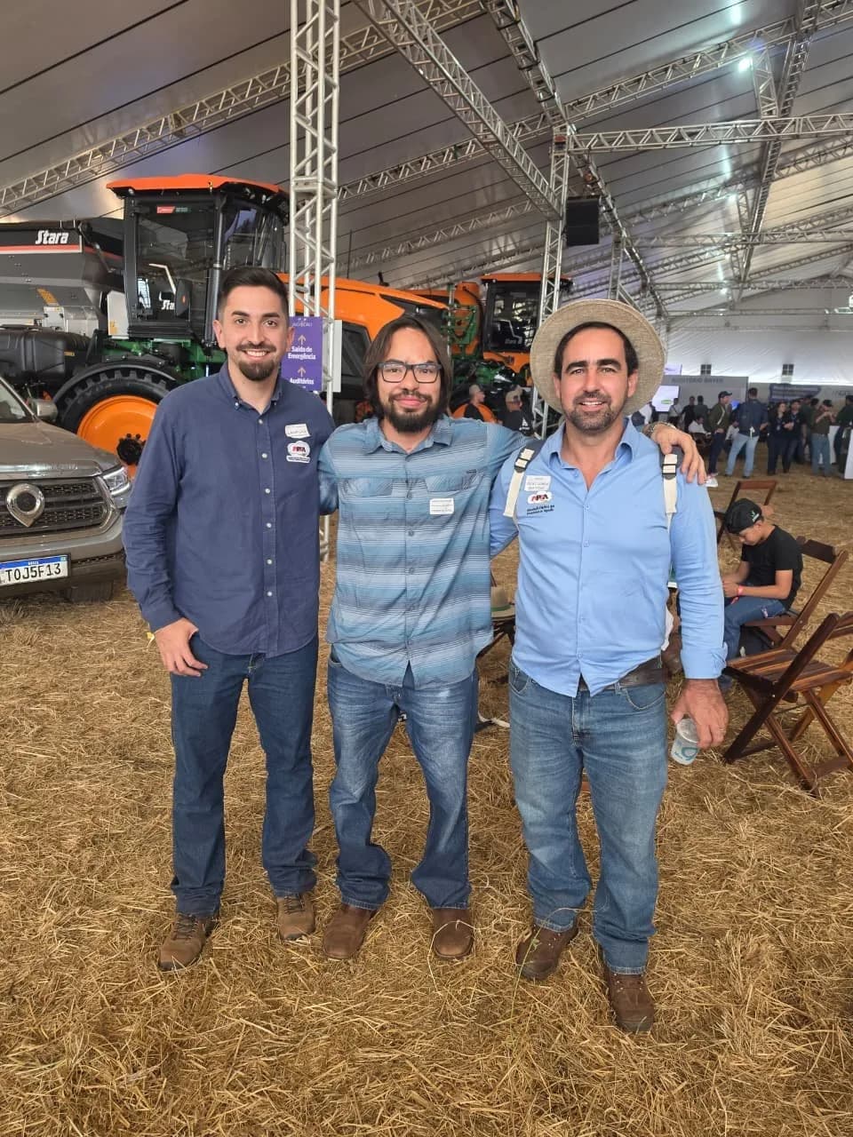 Três participantes em galpão de máquinas agrícolas, com o piso coberto de palha