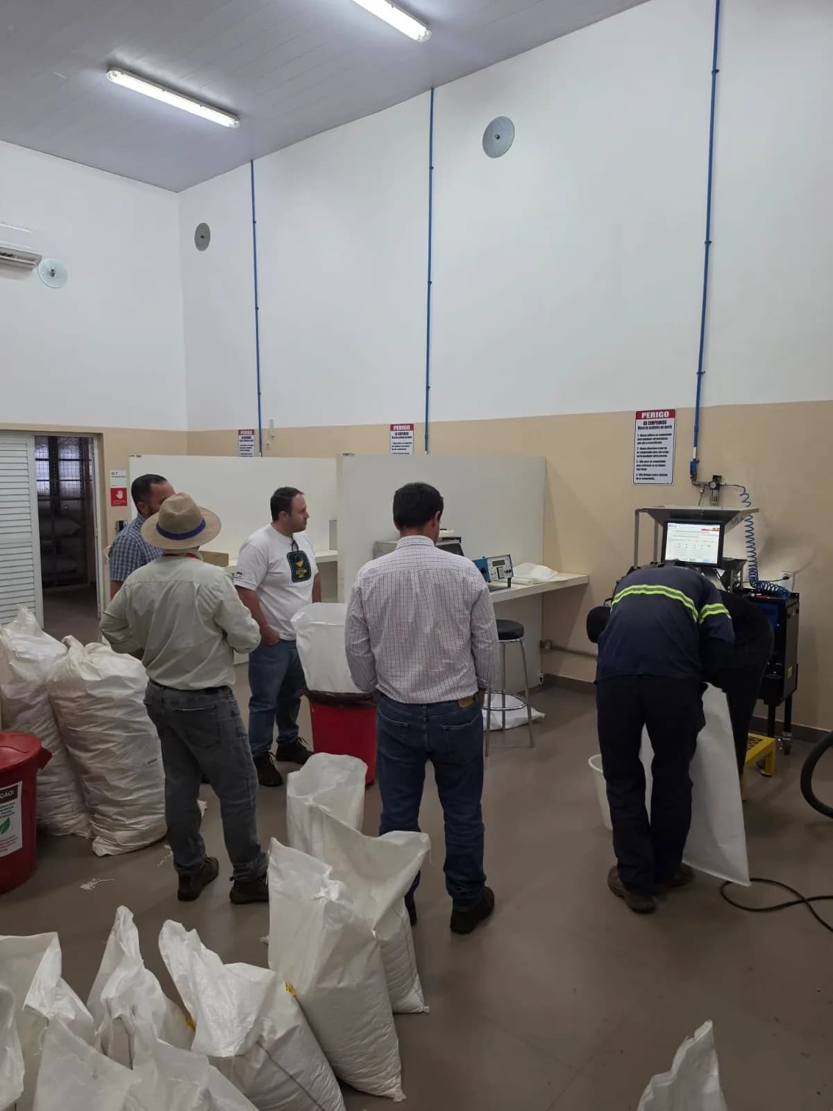Técnicos operando equipamento de análise em laboratório, ao lado de sacos de fibra