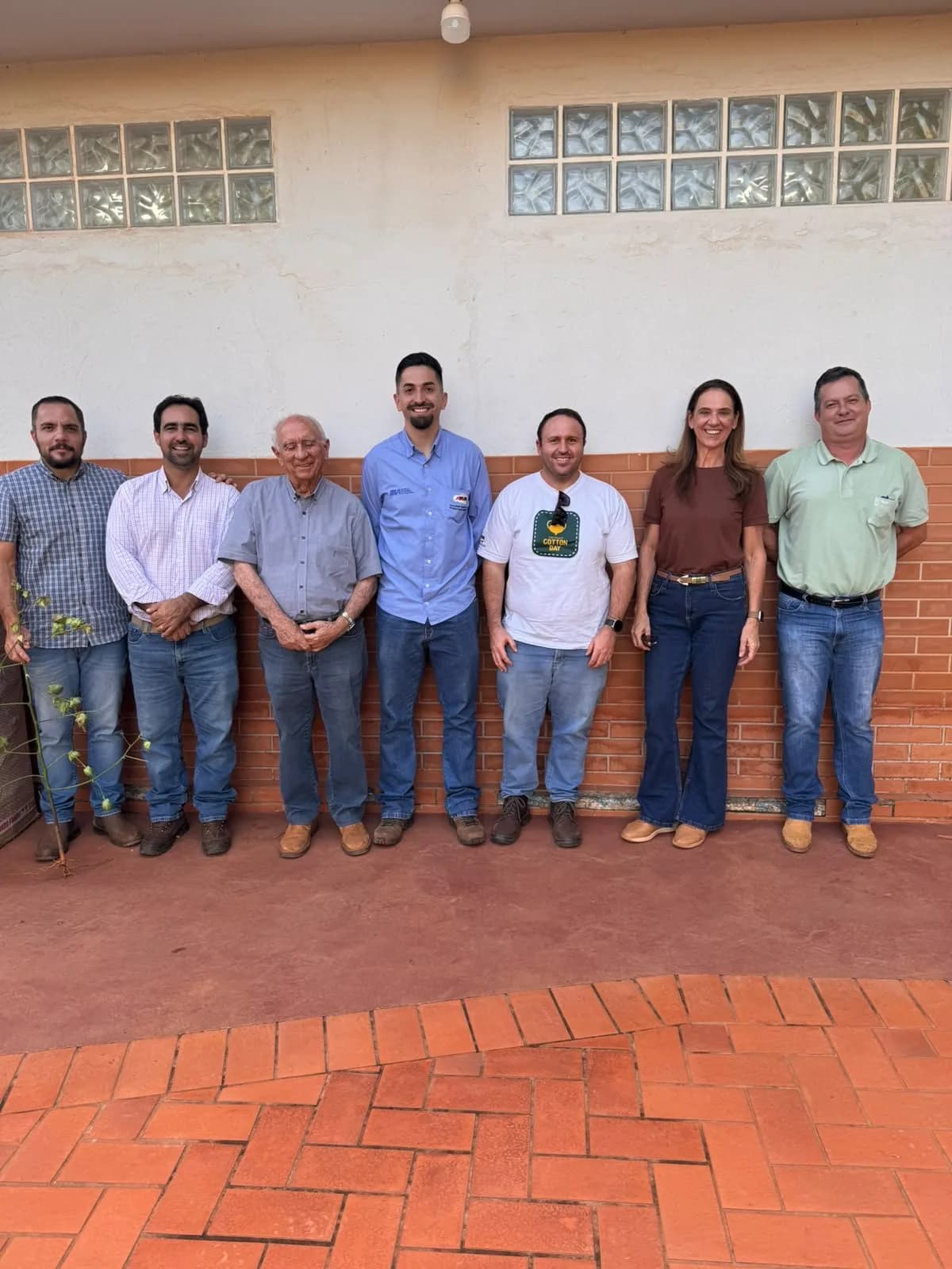 Grupo de sete pessoas diante de uma parede de tijolo aparente