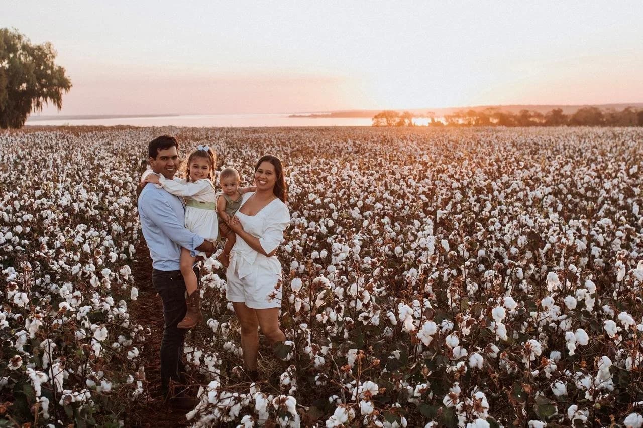 Família com uma criança no colo, em um algodoal ao pôr do sol