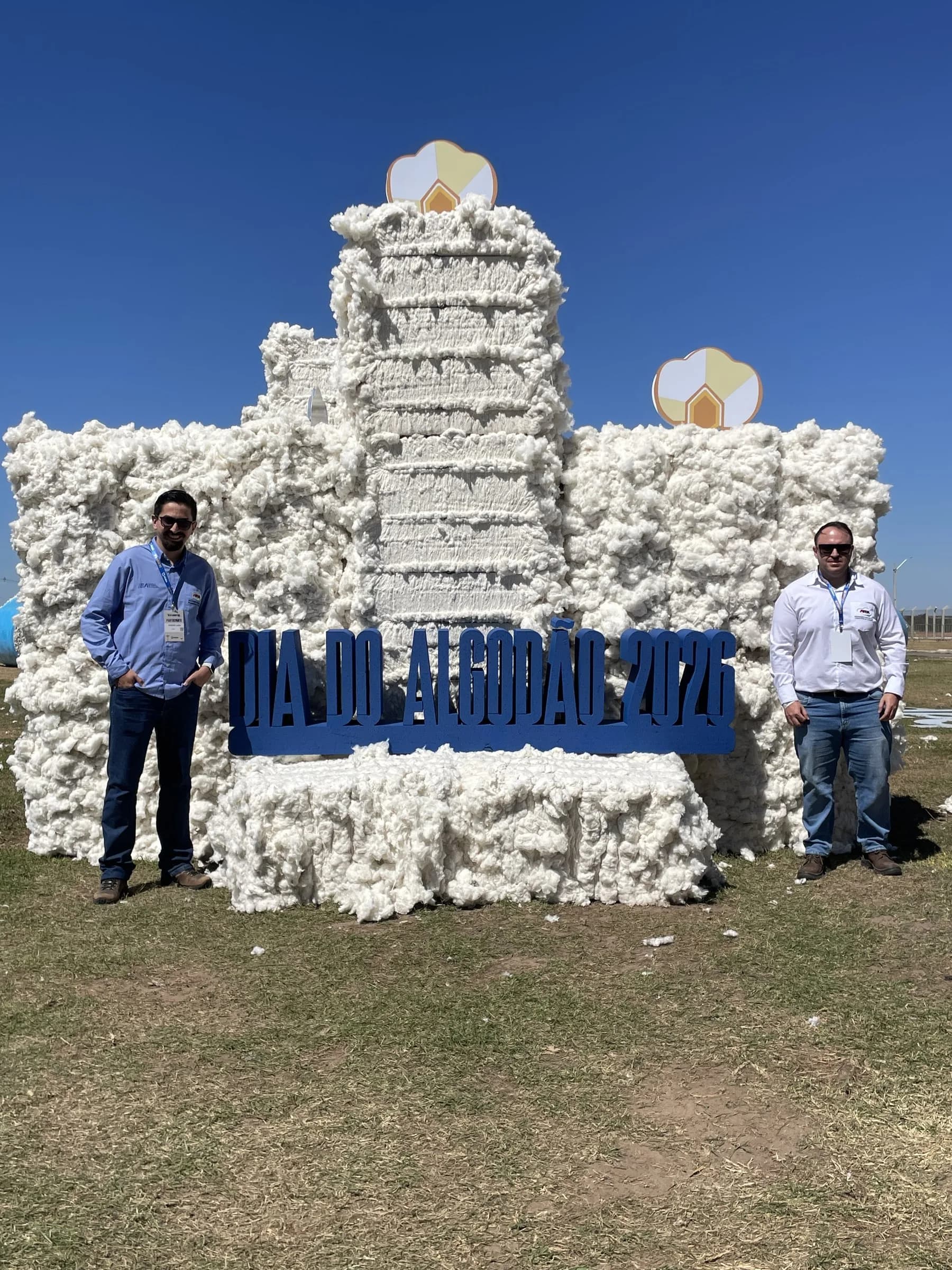 Dois participantes ao lado do letreiro do Dia do Algodão, montado com fardos