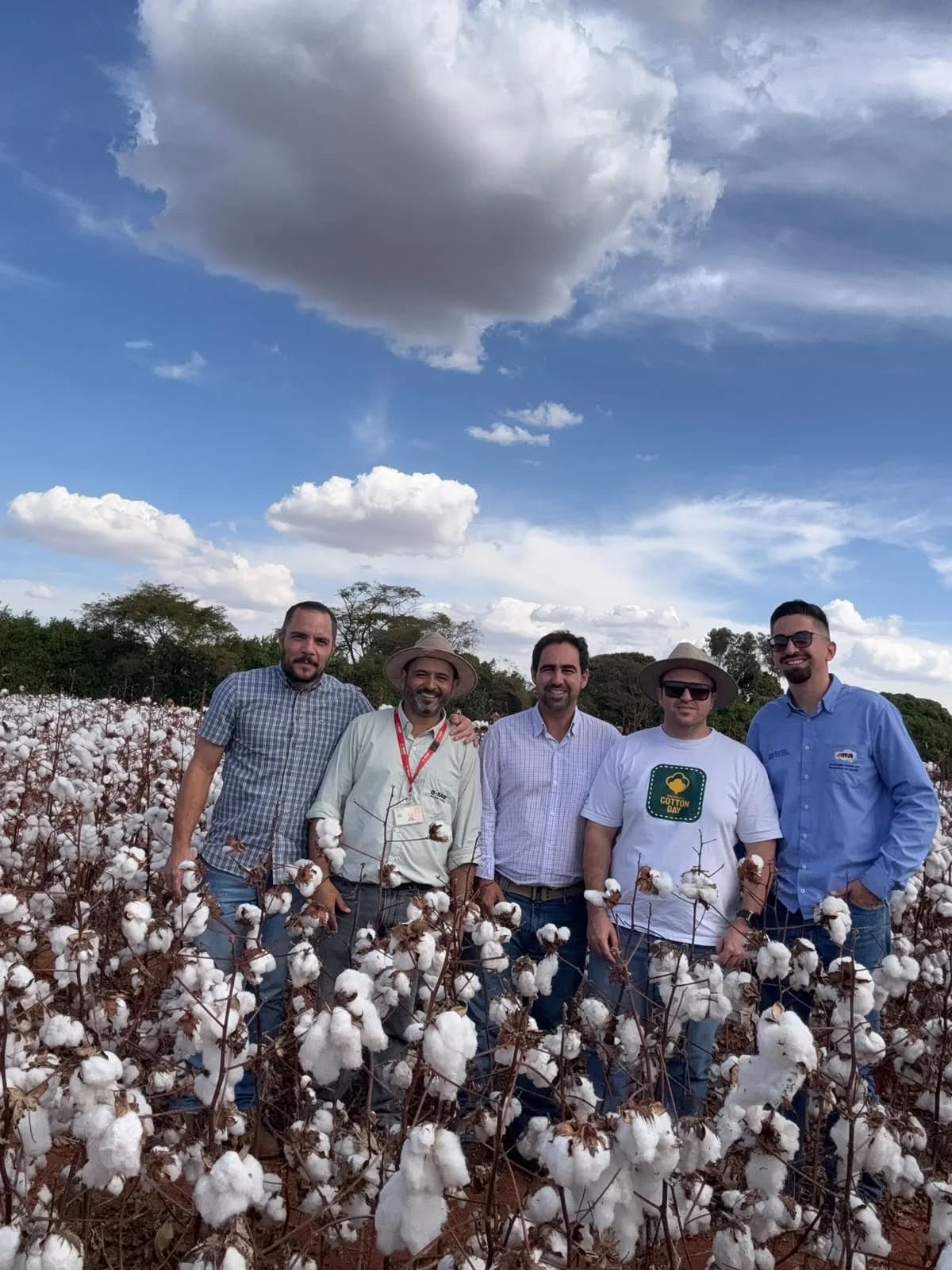 Grupo de cinco pessoas dentro de um algodoal, sob céu de nuvens
